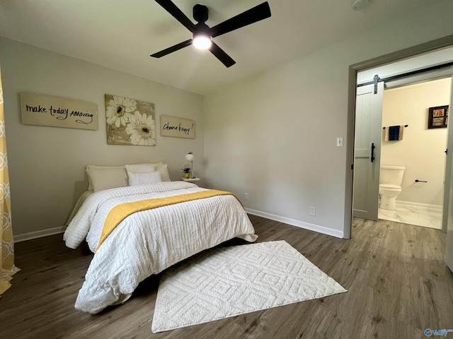 bedroom with ceiling fan, ensuite bathroom, a barn door, wood finished floors, and baseboards