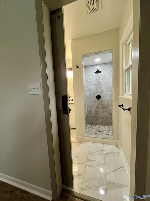 bathroom with a tile shower, visible vents, baseboards, and marble finish floor