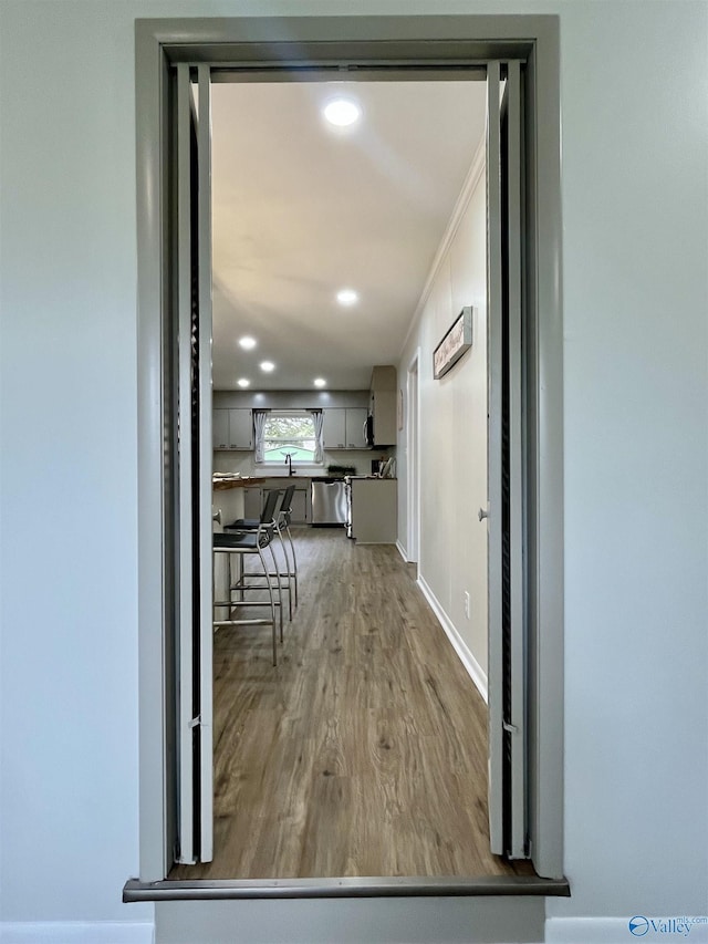 hallway featuring recessed lighting, baseboards, a sink, and wood finished floors