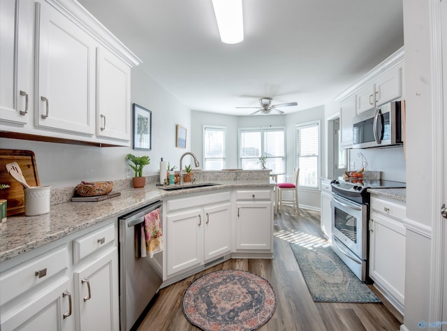 kitchen with a peninsula, wood finished floors, a sink, white cabinets, and appliances with stainless steel finishes