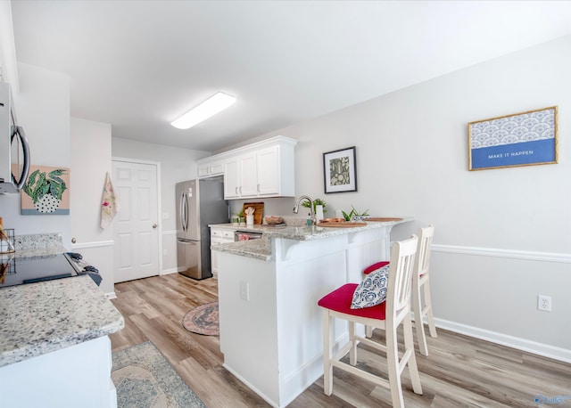 kitchen with a breakfast bar area, freestanding refrigerator, a peninsula, light wood-type flooring, and white cabinetry