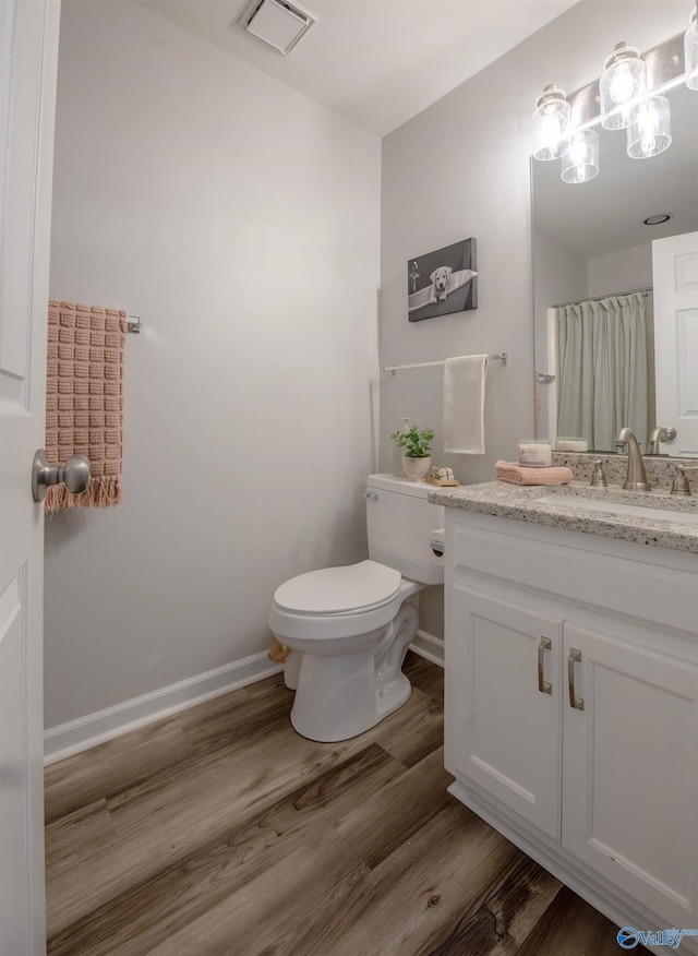 bathroom with toilet, wood finished floors, vanity, visible vents, and baseboards