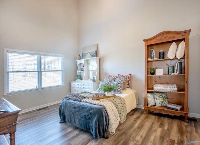 bedroom featuring a high ceiling, visible vents, baseboards, and wood finished floors