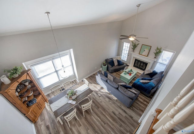 living room with baseboards, a glass covered fireplace, ceiling fan, wood finished floors, and high vaulted ceiling