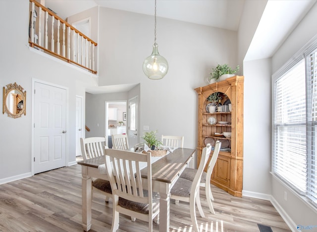 dining room featuring high vaulted ceiling, light wood-style flooring, and baseboards