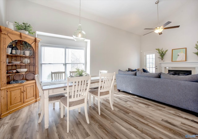 dining space featuring high vaulted ceiling, a fireplace, light wood-style flooring, and ceiling fan