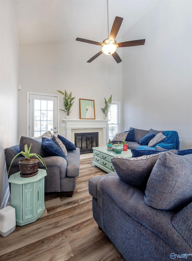 living area with a high ceiling, a ceiling fan, wood finished floors, and a glass covered fireplace