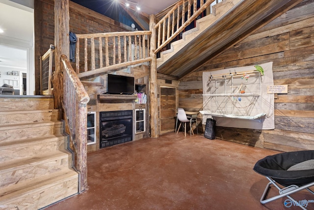 living room with concrete flooring, wooden walls, a fireplace, and stairway