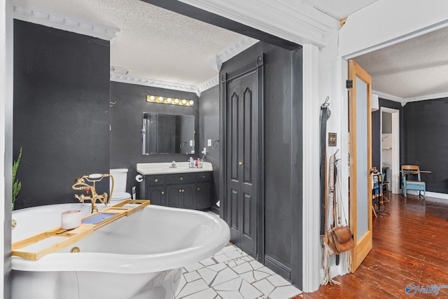 full bath with a textured ceiling, vanity, ornamental molding, wood finished floors, and a jetted tub