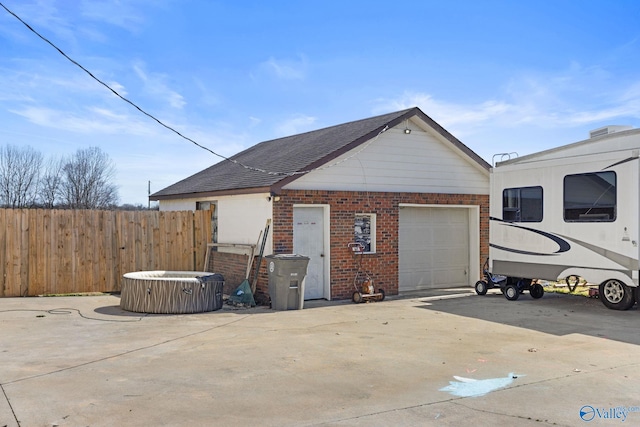 exterior space with a shingled roof, a jacuzzi, fence, concrete driveway, and brick siding