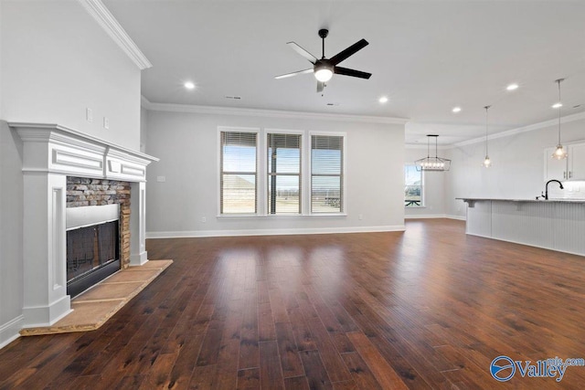 unfurnished living room with ornamental molding, ceiling fan, dark wood-type flooring, sink, and a stone fireplace