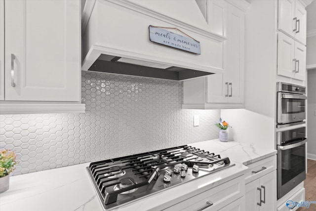 9045 Redstone Square Dr, Huntsville, AL 35824 - kitchen with stainless steel gas stovetop, white cabinets, decorative backsplash, premium range hood, and light stone counters