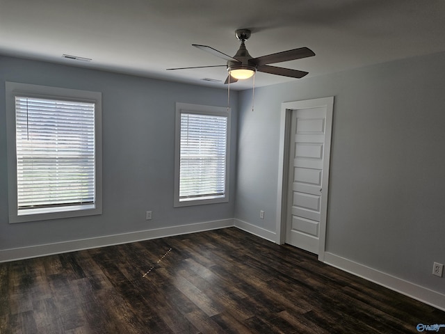 spare room featuring dark wood finished floors, baseboards, visible vents, and ceiling fan