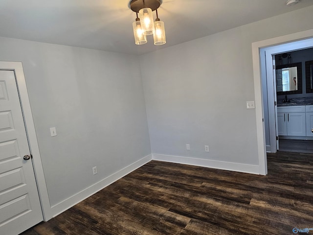 empty room featuring dark wood finished floors, an inviting chandelier, baseboards, and a sink