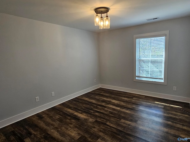 empty room featuring visible vents, baseboards, a notable chandelier, and dark wood-style flooring