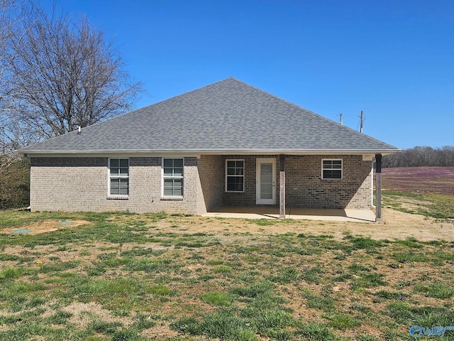 rear view of property featuring a patio area, a lawn, brick siding, and roof with shingles