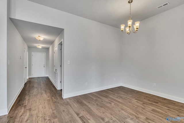 unfurnished dining area with a chandelier, wood finished floors, visible vents, and baseboards