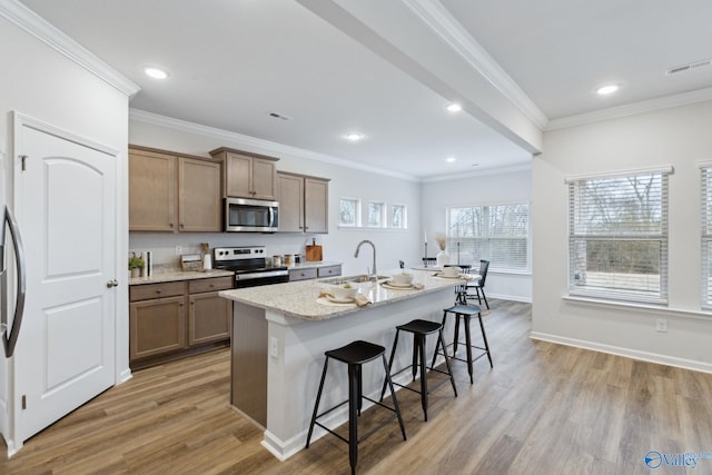 kitchen with sink, a breakfast bar area, light stone counters, an island with sink, and stainless steel appliances