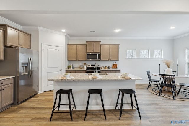 kitchen with appliances with stainless steel finishes, sink, a kitchen island with sink, light stone counters, and light wood-type flooring