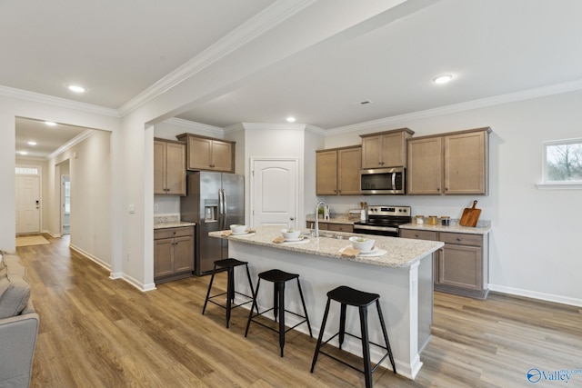 kitchen featuring light hardwood / wood-style flooring, appliances with stainless steel finishes, light stone counters, an island with sink, and a kitchen bar