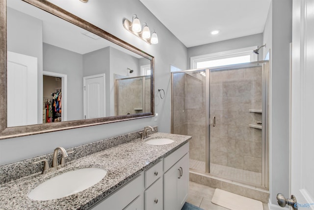 bathroom with a stall shower, double vanity, a sink, and a spacious closet