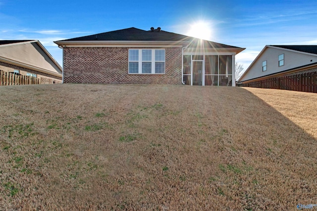 back of property featuring a yard, fence, brick siding, and a sunroom