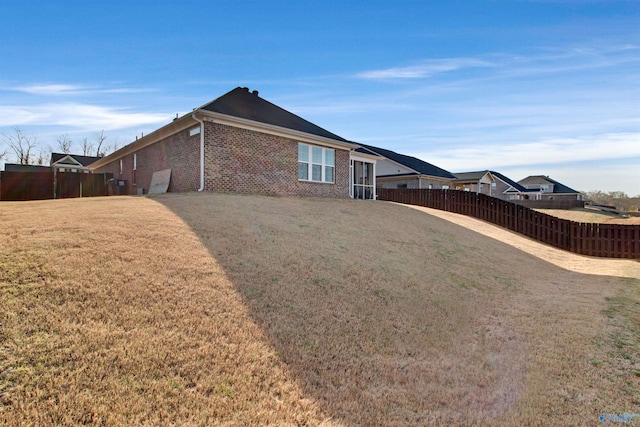 view of property exterior featuring brick siding, fence, and a lawn