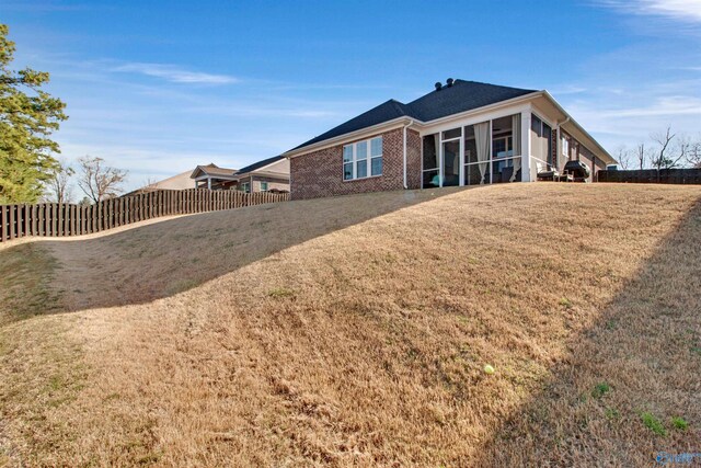 rear view of property with brick siding, a sunroom, fence, and a lawn