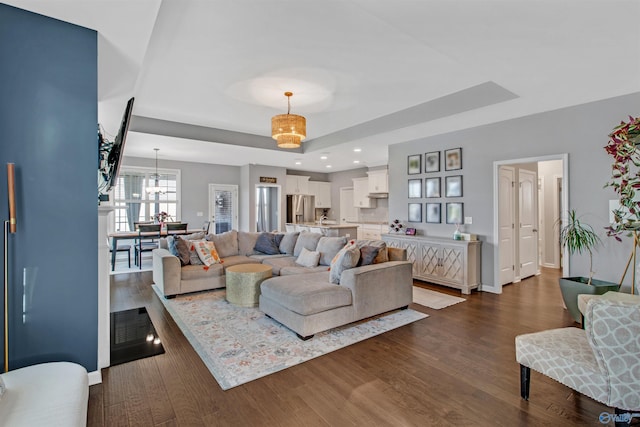 living room with a tray ceiling, dark wood-style flooring, an inviting chandelier, and recessed lighting