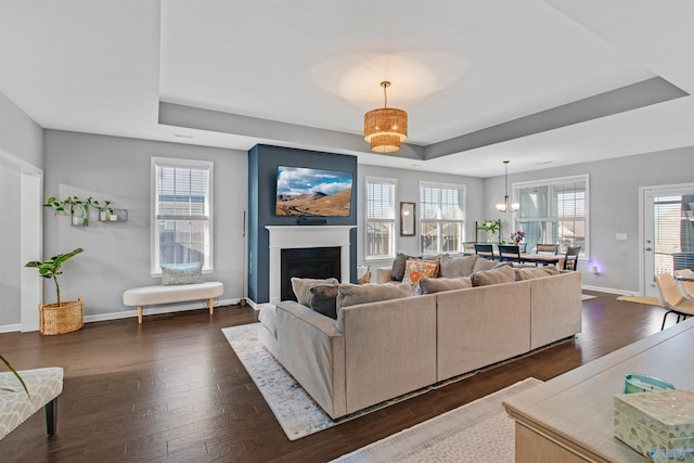 living room featuring dark wood-type flooring, baseboards, a raised ceiling, and a fireplace