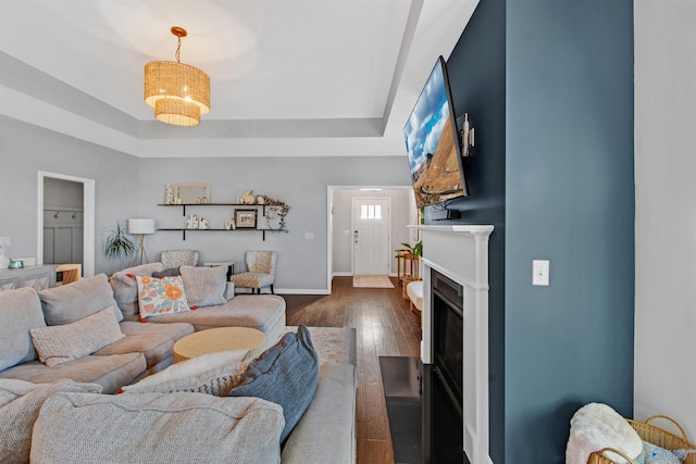living area with a tray ceiling, a fireplace with flush hearth, dark wood-style flooring, and baseboards