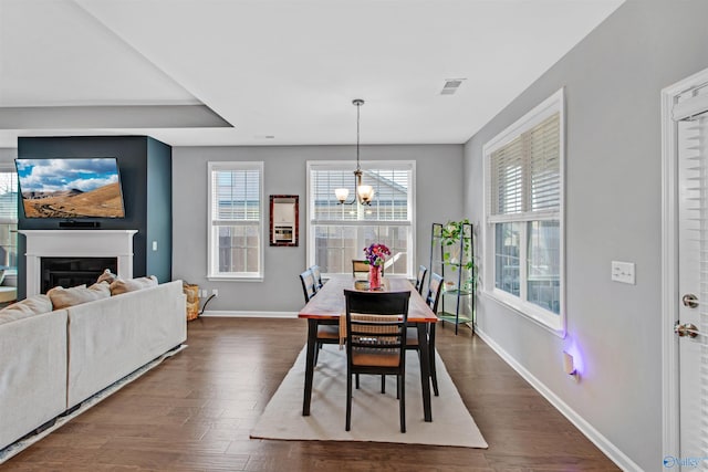 dining area featuring baseboards, a notable chandelier, a fireplace, and dark wood finished floors