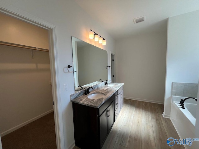 bathroom with tiled bath, vanity, and wood-type flooring