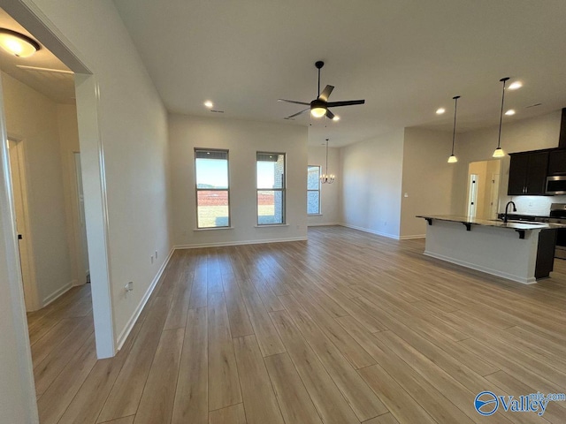 unfurnished living room with light hardwood / wood-style floors, sink, and ceiling fan with notable chandelier