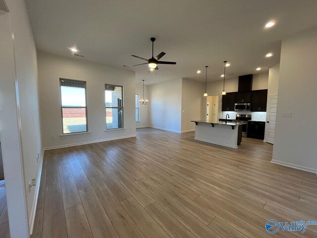 unfurnished living room featuring ceiling fan with notable chandelier and light hardwood / wood-style flooring