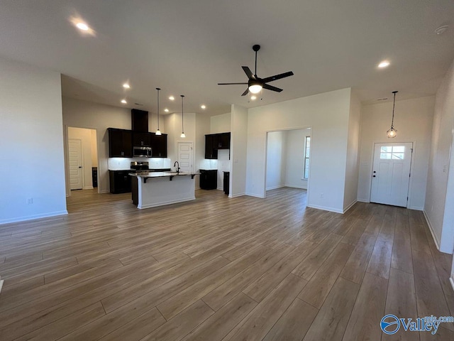 unfurnished living room with ceiling fan, a towering ceiling, hardwood / wood-style floors, and sink