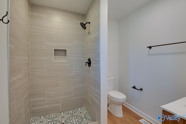 bathroom with hardwood / wood-style flooring, vanity, a tile shower, and toilet