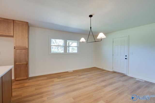 unfurnished dining area featuring an inviting chandelier and light hardwood / wood-style flooring