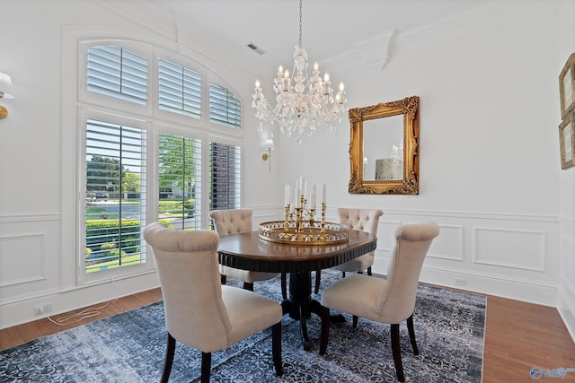 dining room with a chandelier, a decorative wall, ornamental molding, wainscoting, and wood finished floors