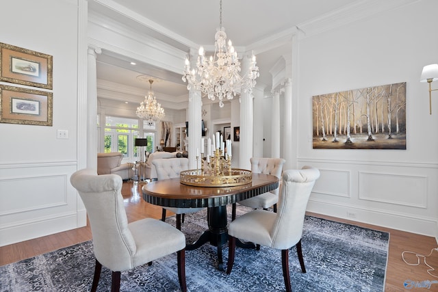 dining room featuring a chandelier, crown molding, wood finished floors, a decorative wall, and decorative columns