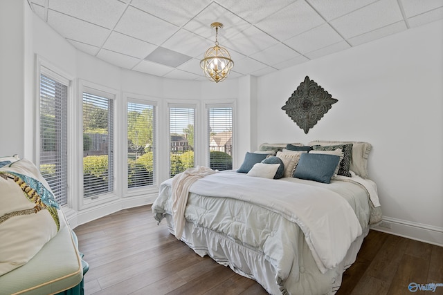 bedroom with a drop ceiling, dark wood-type flooring, a chandelier, and baseboards