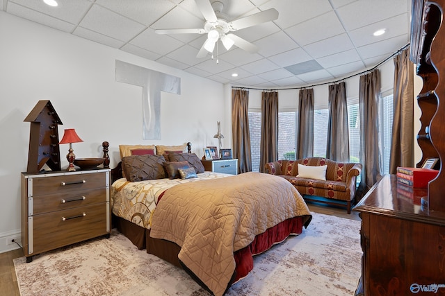 bedroom featuring a drop ceiling, light wood-style flooring, and ceiling fan