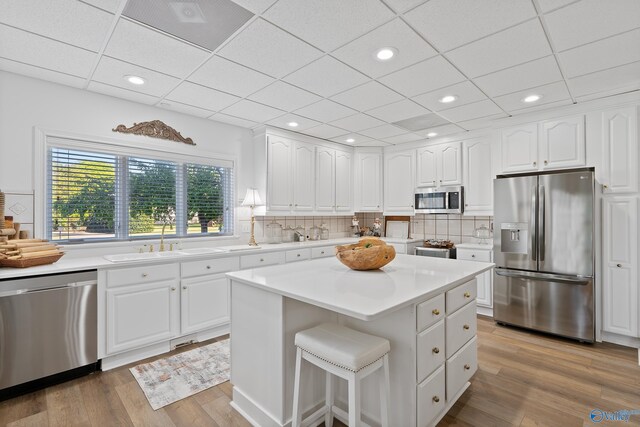 kitchen featuring appliances with stainless steel finishes, a sink, light wood-type flooring, tasteful backsplash, and white cabinetry