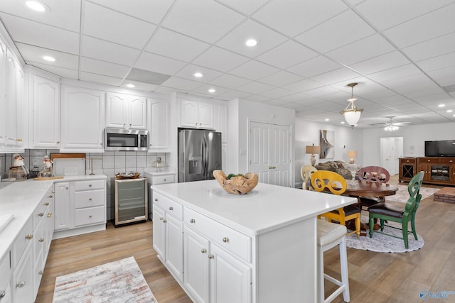 kitchen with appliances with stainless steel finishes, wine cooler, light wood finished floors, white cabinetry, and open floor plan