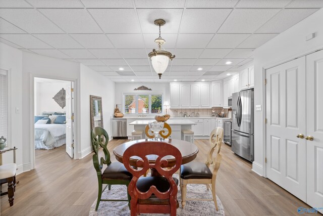 dining area featuring light wood-type flooring, baseboards, and a paneled ceiling