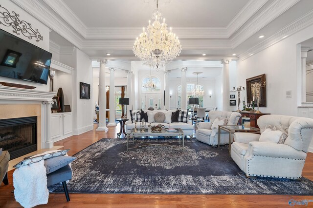 living room featuring ornate columns, a chandelier, wood finished floors, crown molding, and a fireplace