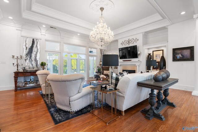 living area featuring a chandelier, hardwood / wood-style flooring, ornamental molding, a tray ceiling, and baseboards