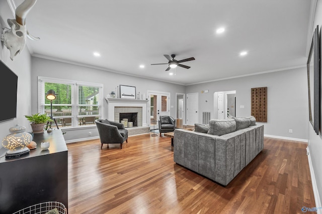 living room featuring a brick fireplace, a ceiling fan, crown molding, and wood finished floors