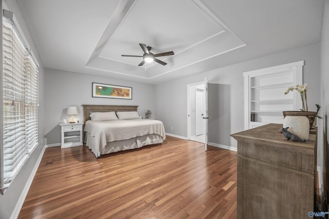 bedroom with baseboards, a ceiling fan, a tray ceiling, and wood finished floors