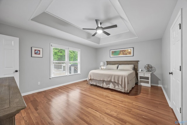 bedroom featuring ceiling fan, a raised ceiling, baseboards, wood finished floors, and visible vents